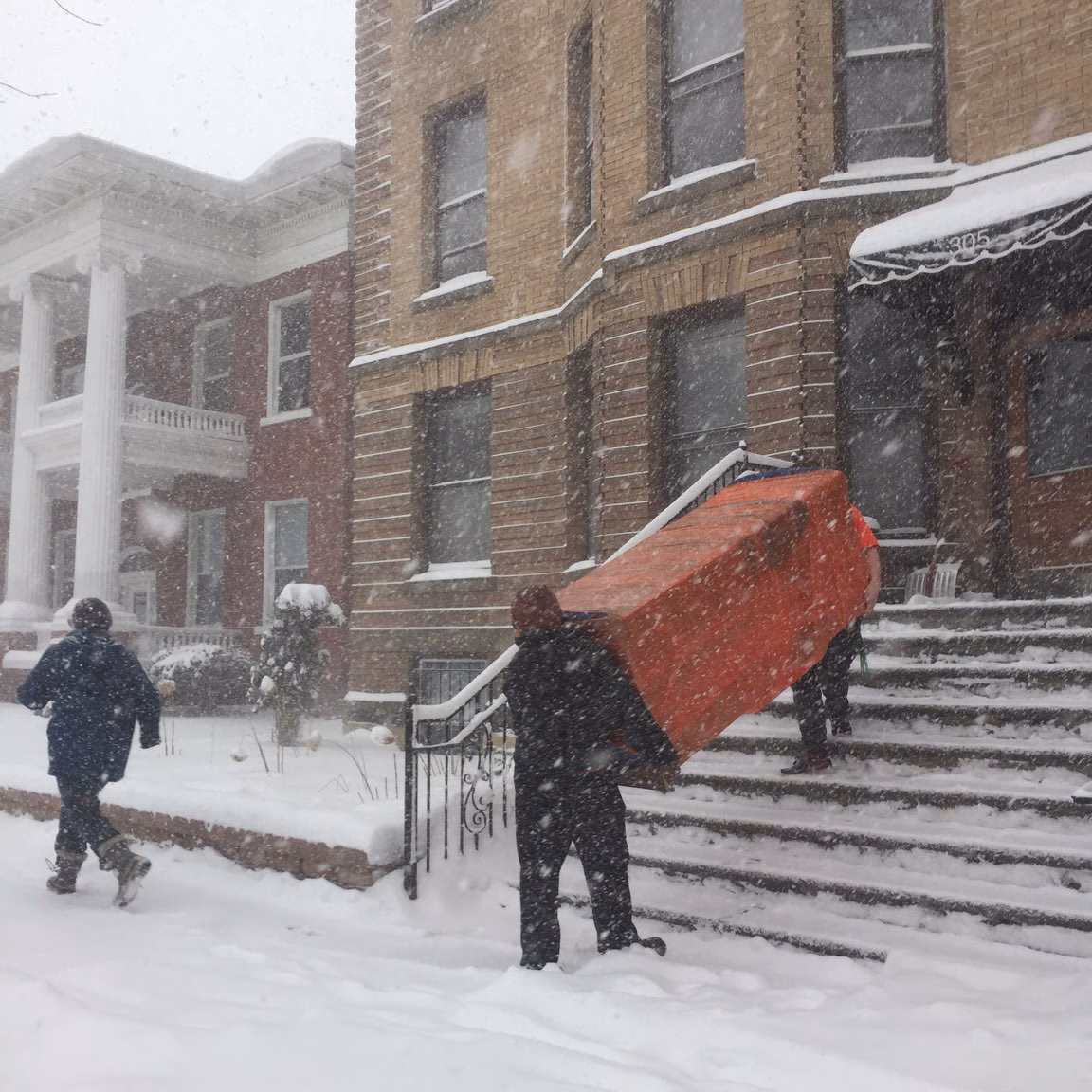 Two movers carrying a piece of large furniture outside in the snow