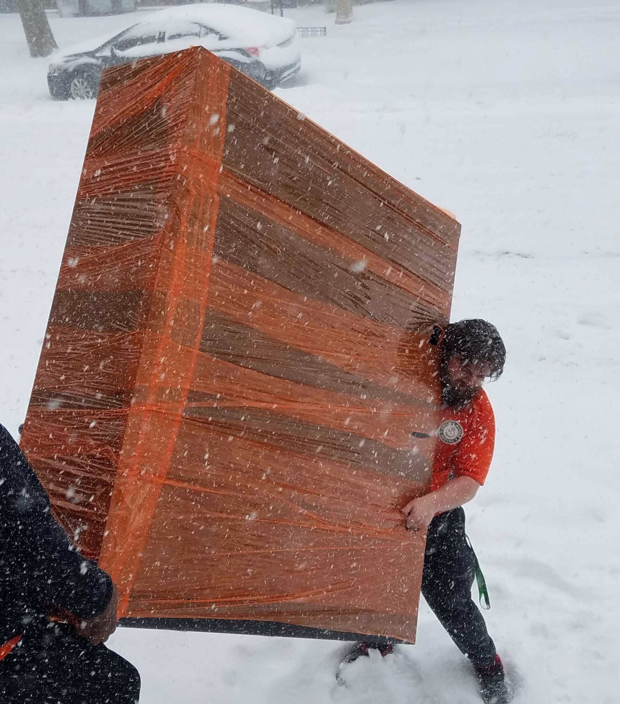Two movers carrying a piece of large furniture outside in the snow