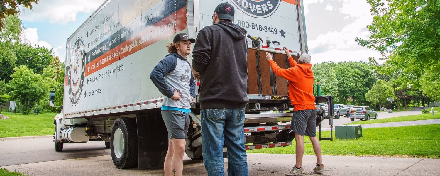 A mover walking up the ramp of a College Muscle Moves truck on a snowy residential street in Minneapolis, MN