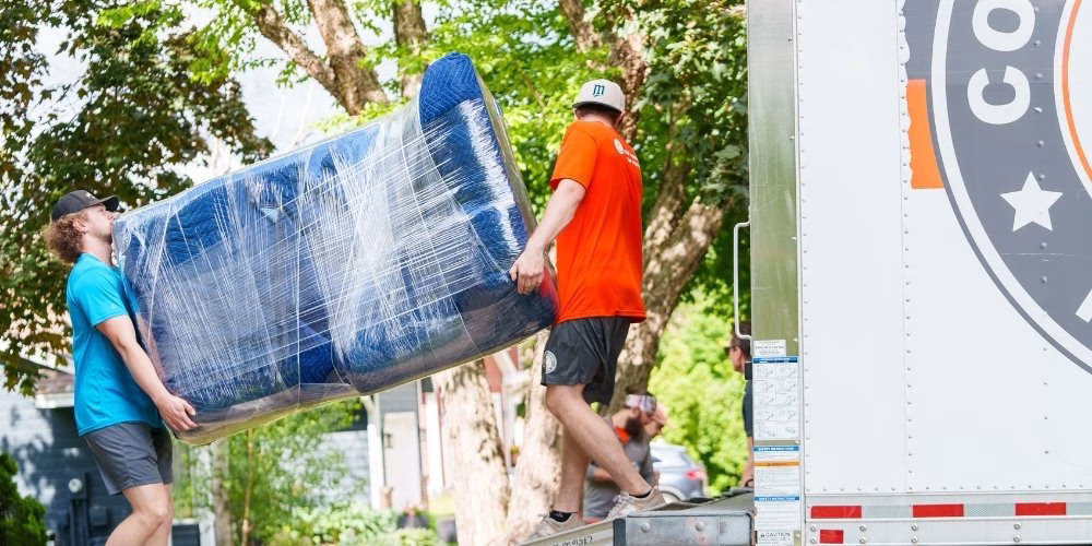 A pair of College Muscle Movers carrying a wrapped sofa up a moving truck ramp in Saint Paul, MN