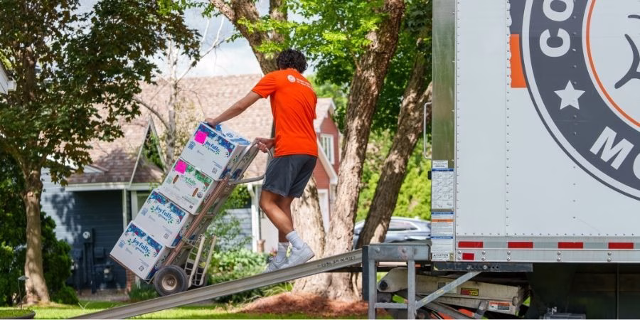 A College Muscle Movers employee pulling a stack of boxes into a truck with a dolly outside a house near Minneapolis, MN