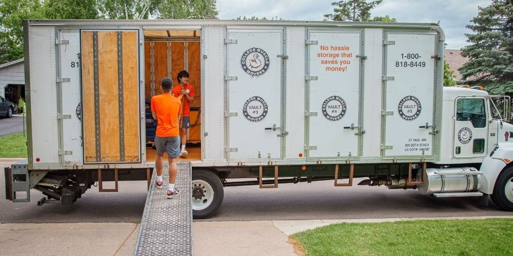 Two College Muscle Movers employees carrying furniture out of a truck at a house near Minneapolis, MN