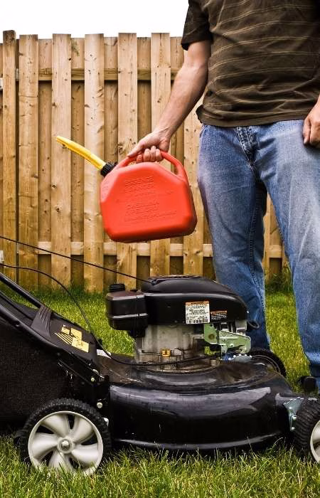 Moving Gas-Powered Lawnmowers A man in his yard holding a gas can next to a push lawnmower.