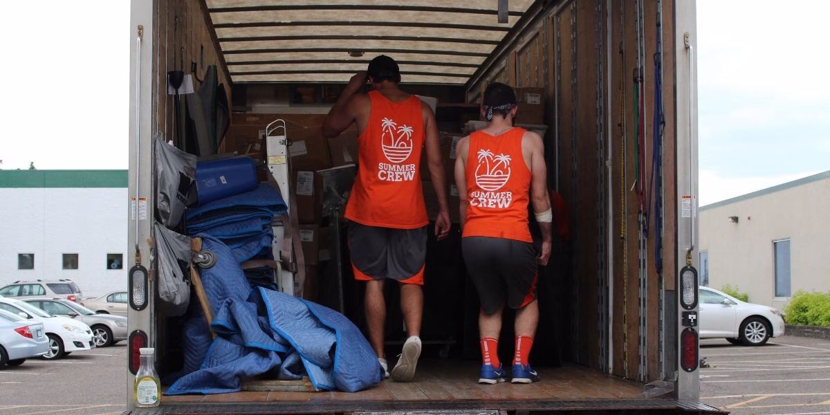Two College Muscle Movers employees moving items out of a truck during a summer move.