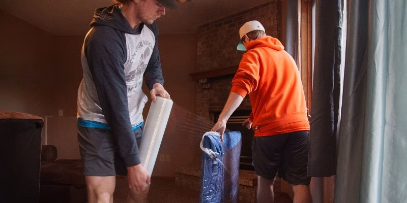 A pair of College Muscle Movers employees padding and wrapping a TV for transit.