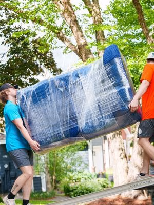A pair of College Muscle Movers carrying a wrapped sofa up a moving truck ramp in Saint Paul, MN